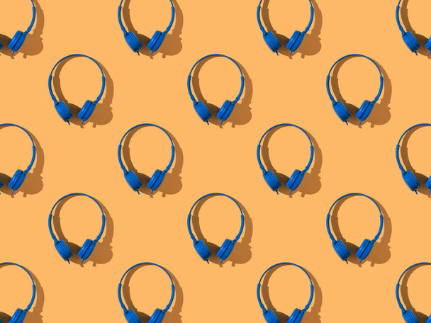 Vzor jasně modrých sluchátek na oranžovém pozadí. Mobilní zařízení pro přehrávání zvuku. - Fotografie, Obrázek