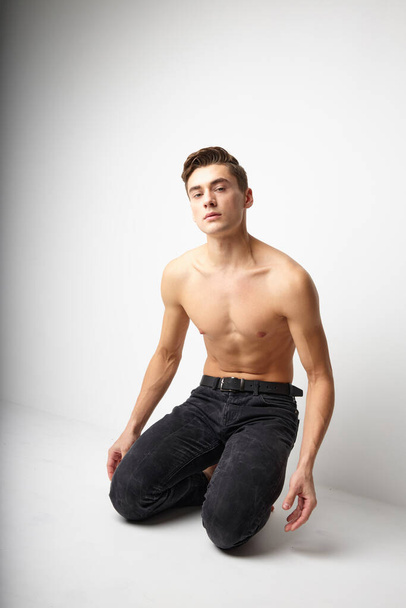 A man with a naked torso is kneeling studio posing attractive look - Фото, изображение