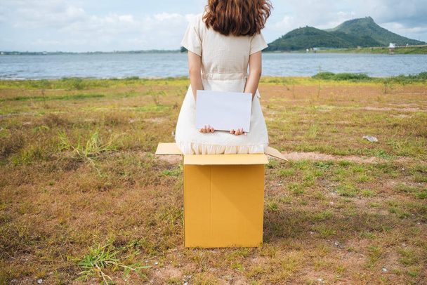 Vissza nézet - Fiatal ázsiai thai nő hipster göndör frizura fehér ruha kezében üres papír jel mögött a doboz a tónál. Fénymásolási hely. - Fotó, kép