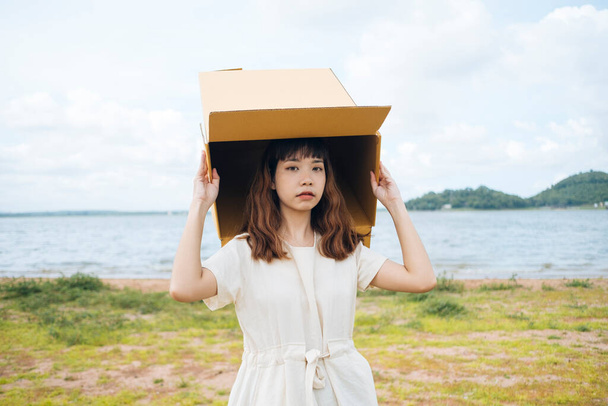 Молодая азиатская тайка хипстер кудрявая прическа на белом платье играет с картонной коробкой положить над головой на озере. - Фото, изображение