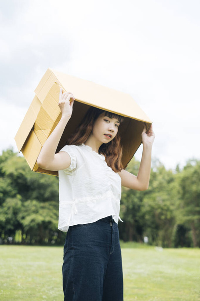 jong aziatische thai vrouw hipster krullend kapsel op wit shirt cover hoofd met kartonnen doos. - Foto, afbeelding