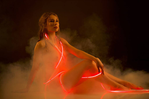Graceful naked woman with red neon light stripe in studio - Foto, imagen