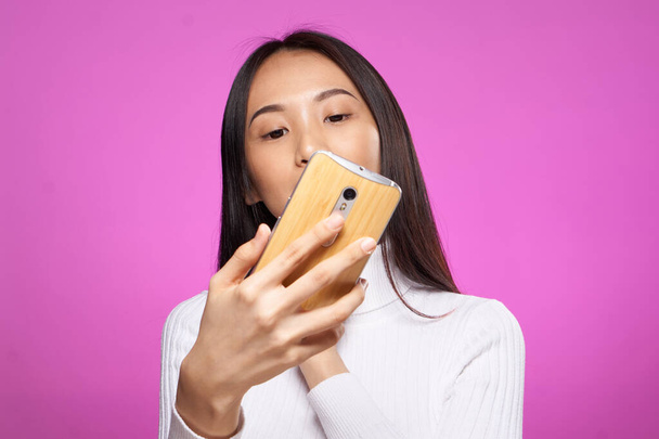 aziatische vrouw op zoek naar telefoon internet technologie roze achtergrond - Foto, afbeelding