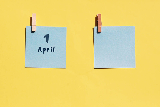 1. April. Tag eines Monats, Kalenderdatum. Zwei blaue Blätter zum Schreiben auf gelbem Hintergrund. Draufsicht, Kopierraum. Frühlingsmonat, Tag des Jahres - Foto, Bild