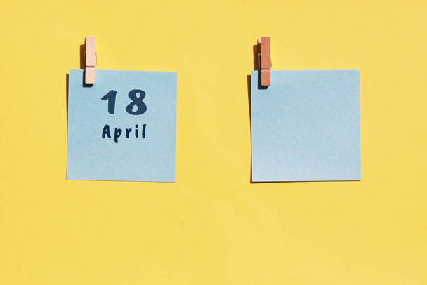 Am 18. April. Tag des 18. Monats, Kalenderdatum. Zwei blaue Blätter zum Schreiben auf gelbem Hintergrund. Draufsicht, Kopierraum. Frühlingsmonat, Tag des Jahres - Foto, Bild