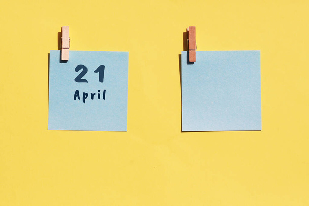 21. April. Tag des 21. Monats, Kalenderdatum. Zwei blaue Blätter zum Schreiben auf gelbem Hintergrund. Draufsicht, Kopierraum. Frühlingsmonat, Tag des Jahres - Foto, Bild
