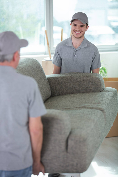 delivery men moving sofa in room at new home - Foto, imagen