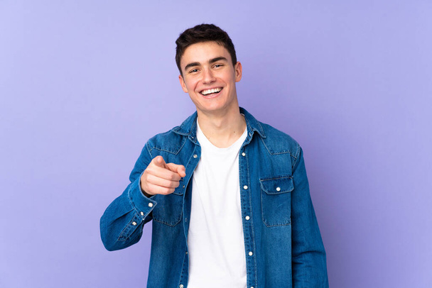 Teenager caucasian  handsome man isolated on purple background surprised and pointing front - Photo, Image