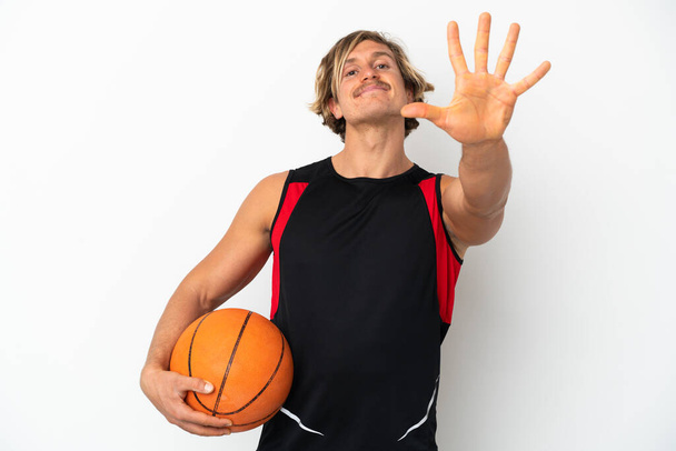 Νεαρός ξανθός άντρας κρατά μια μπάλα του μπάσκετ απομονωμένος σε λευκό φόντο μετρώντας πέντε με τα δάχτυλα - Φωτογραφία, εικόνα