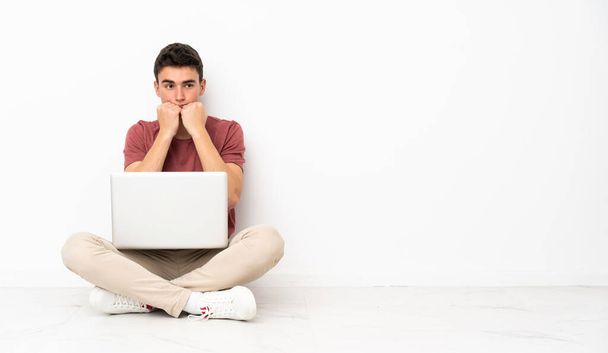 Подросток сидит на флоре с ноутбуком нервничает и боится положить руки в рот - Фото, изображение