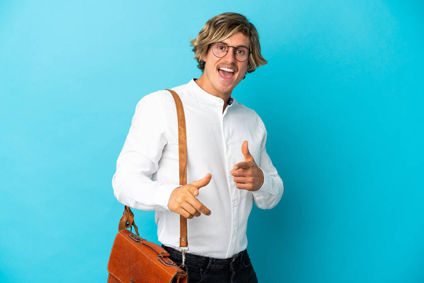 Young blonde businessman isolated on blue background pointing to the front and smiling - 写真・画像