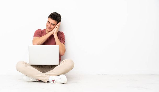 Teenager man sitting on the flor with his laptop making sleep gesture in dorable expression - Photo, Image