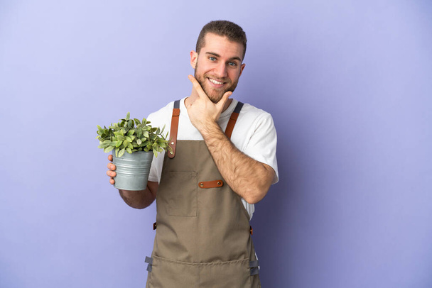 Gardener caucasian man holding a plant isolated on yellow background happy and smiling - Photo, Image