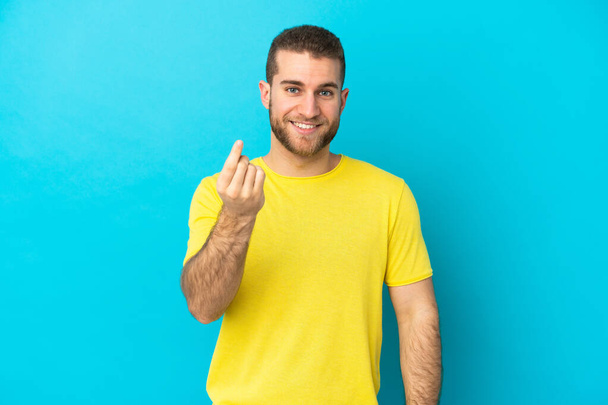 Young handsome caucasian man isolated on blue background making money gesture - Φωτογραφία, εικόνα
