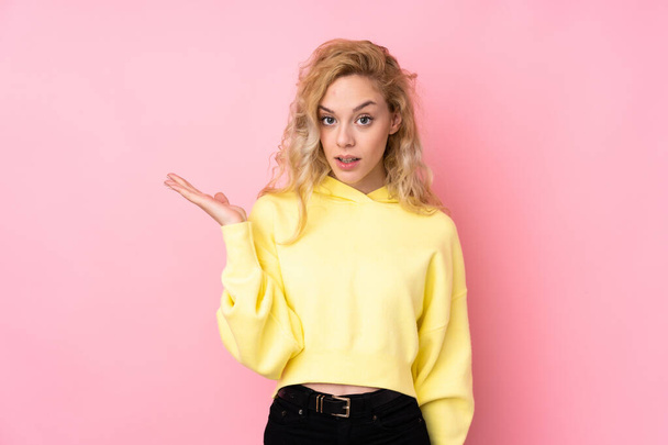 Young blonde woman wearing a sweatshirt isolated on pink background making doubts gesture - Zdjęcie, obraz