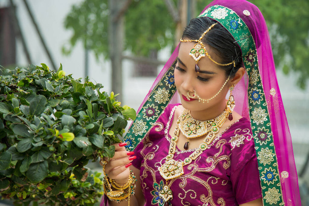 Середній зблизька портрет азіатка в пурпуровій індійській традиції сарі, витискаючи руку зеленій тропічній рослині. - Фото, зображення