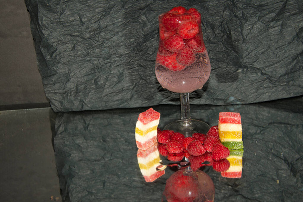 wineglass with champagne with raspberries and sweets on light background, romantic concept  - Photo, Image