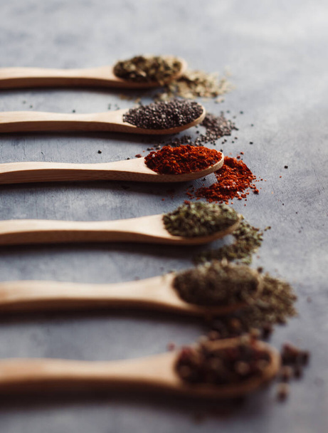 A vertical shot of assortment of spices on wooden spoons: chia, paprika, parsley, rosemary, and tea - Zdjęcie, obraz