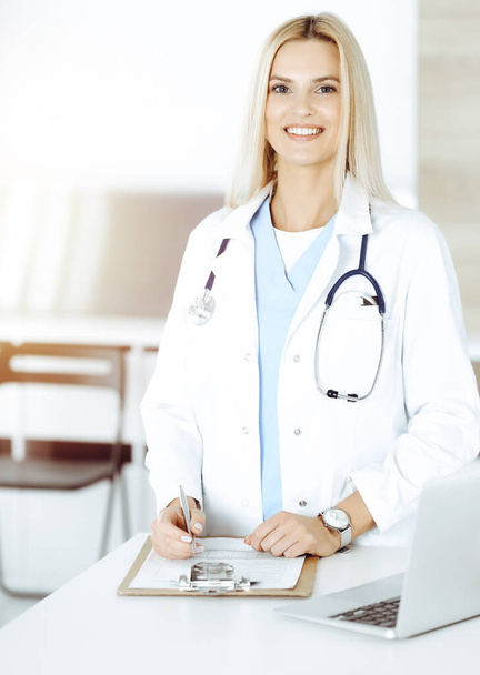 Doctor woman controls medication history records and exam results while using clipboard in sunny hospital . Medicine and healthcare concept - Foto, Bild