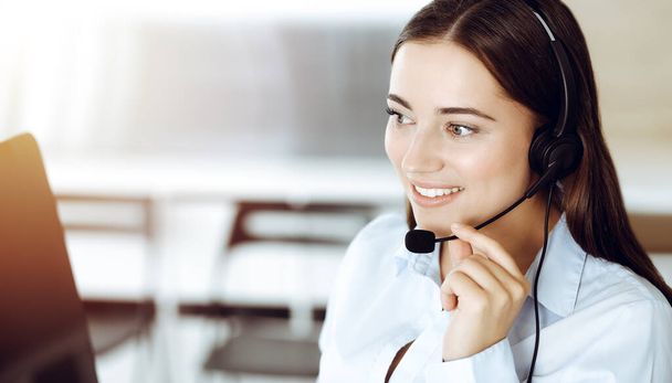 Brunette vrouwelijke klantenservice vertegenwoordiger met behulp van headset en consulting klanten online. Oproepcentrum - Foto, afbeelding