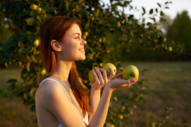 счастливая женщина с зелеными яблоками в руках в природе рядом с деревом на лугу - Фото, изображение