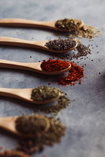 A vertical shot of assortment of spiceson wooden spoons: chia, paprika, parsley, rosemary, and teas - Zdjęcie, obraz
