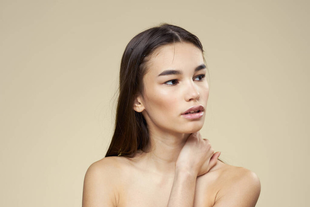 Woman with bared shoulders dark hair clean skin makeup beige background - Фото, зображення