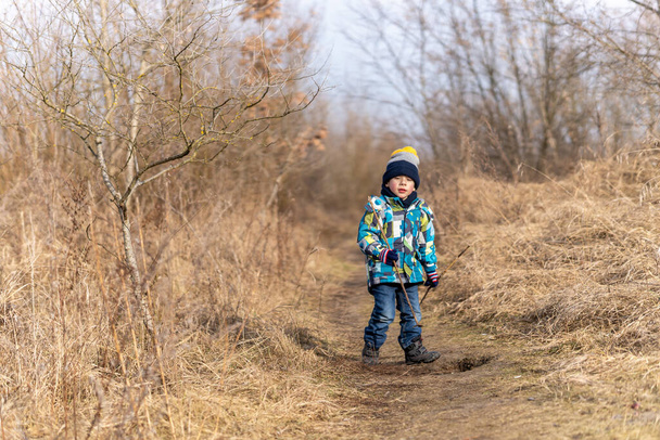 POZNAN, POLAND - Feb 06, 2021: Young boy walking along dry shrubs and grass at a park on a cold winter day. - Fotografie, Obrázek