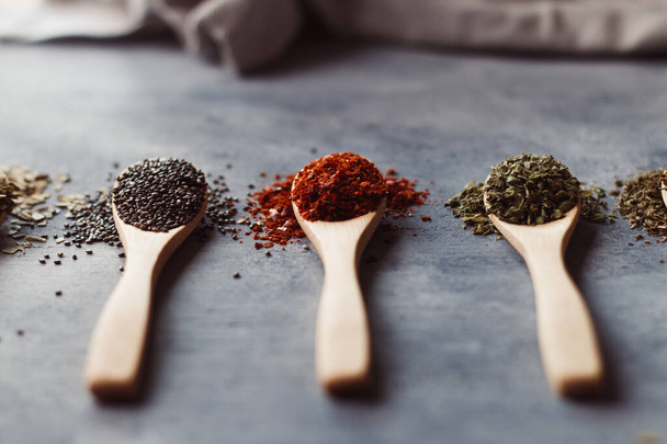 A selective focus shot of assortment of spices on wooden spoons: chia, paprika, and parsley - Foto, Imagen