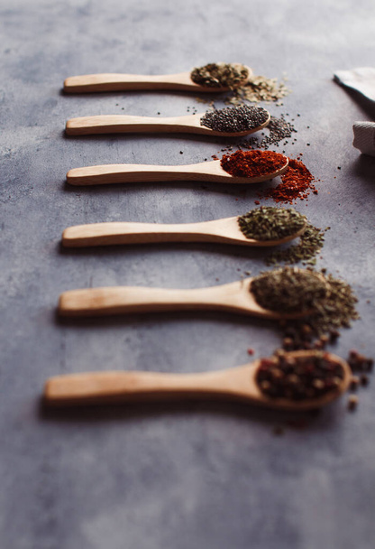 A vertical shot of assortment of spiceson wooden spoons: chia, paprika, parsley, rosemary, and teas - Foto, imagen