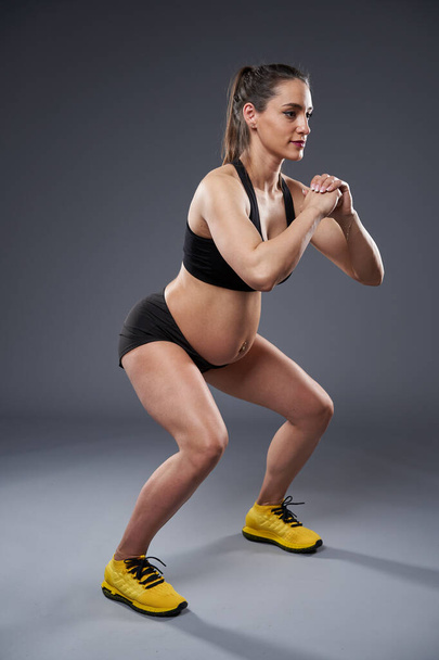Young pregnant woman doing fitness exercise, studio shot on gray background - Foto, Imagem