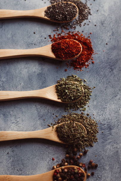 A vertical shot of assortment of spices on wooden spoons: chia, paprika, parsley, rosemary, and tea - 写真・画像
