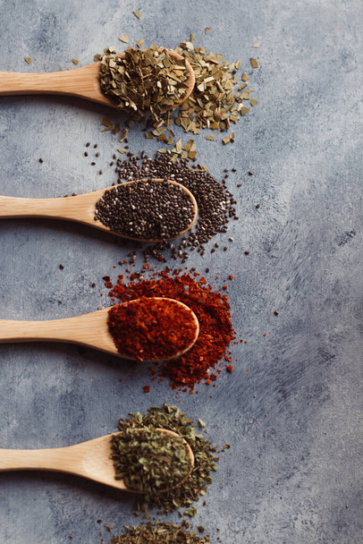 A vertical shot of assortment of spices on wooden spoons: chia, paprika, parsley, anrosemary - Foto, immagini