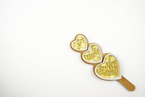 Yellow capsules of Omega 3 lie on white ceramic plates in the form of the hearts - Foto, immagini