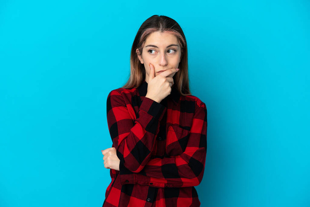 Young caucasian woman isolated on blue background having doubts and with confuse face expression - Foto, afbeelding