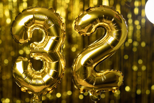 Die goldene Zahl 32 32 besteht aus einem aufblasbaren Ballon auf gelbem Grund. Eine der vollständigen Zahlen. Geburtstag, Jubiläum, Datumskonzept - Foto, Bild