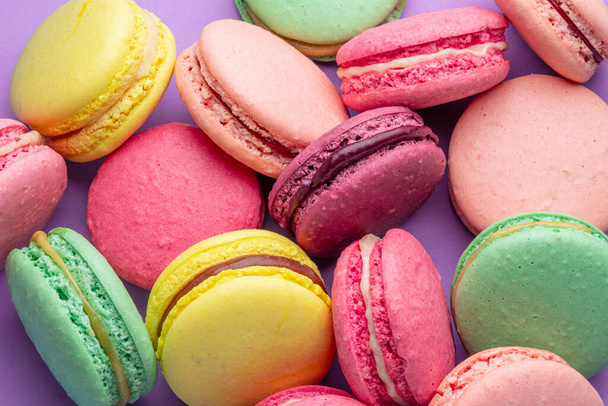 Colorful sweet macarons or macaroons, flavored cookies on purple background. - Фото, изображение