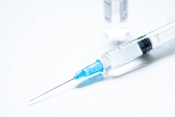 Syringe with needle without cover or top, vial or phial on a white empty space background ready to be used. Covid or Coronavirus vaccine or monoclonal antibodies background, close up - Photo, Image