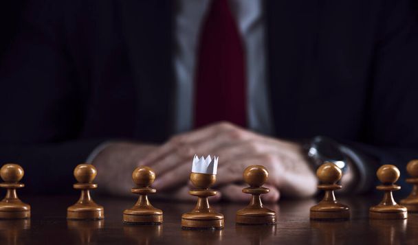 the concept of strategy and business planning, a businessman at a chessboard in front of lined up white pawns, one of which is in a paper crown, strategy and tactics, readiness for battle. - Fotografie, Obrázek