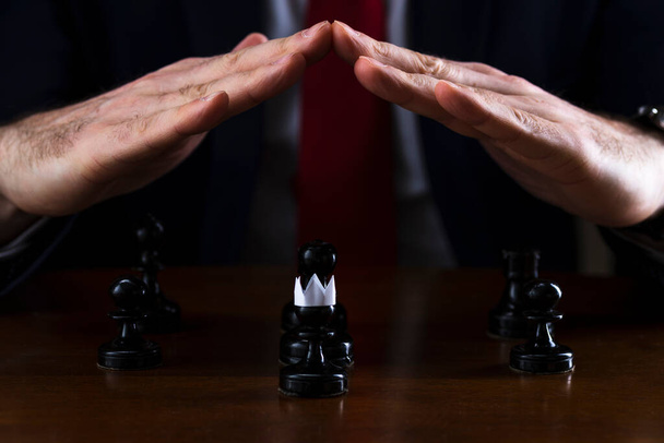 the concept of strategy and business planning, a businessman at a chessboard in front of lined black pawns, one of which is in a paper crown, strategy and tactics, readiness for battle - Фото, изображение