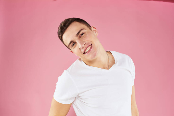 A man in a white t-shirt gestures with his hands emotions pink background studio cropped view - Photo, Image
