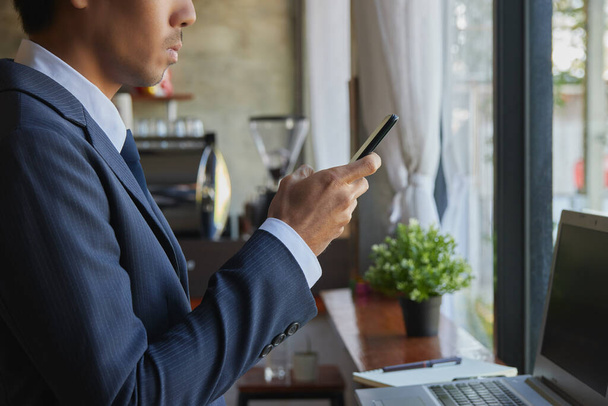 Right View Álló ázsiai üzletember öltönyben Mobiltelefon és laptop használata a kávézóban jelenet. Ázsiai üzletember Munka bárhonnan a technológiával - Fotó, kép
