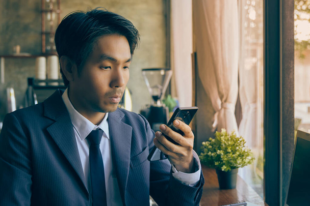Предприниматель из Азии в костюме и галстуке в кофейне. Азиатский бизнесмен работает из любого места с технологиями в винтажном тоне - Фото, изображение