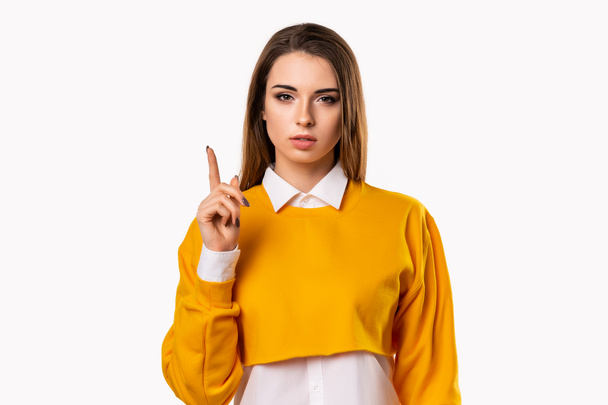 Portrait of Serious brunette girl showing index finger, scolding or telling off someone. Girl raises finger up, says: Attention please - Photo, image