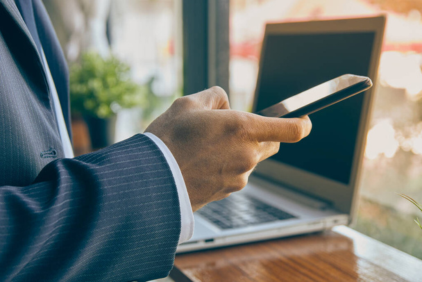 Zoom View Hand of Businessman in Suit Okostelefon vagy mobiltelefon használata Laptop háttér a kávézóban jelenet. Üzletember Munka bárhol a technológia Vintage Tone - Fotó, kép