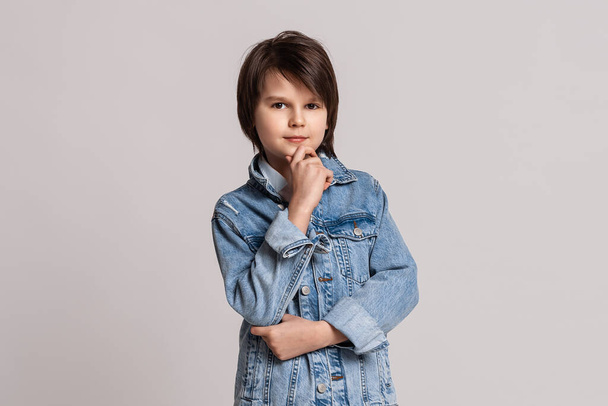Jóképű, divatos kisfiú, 11-13 éves, farmerdzsekiben pózol a stúdióban. Modell teszt. Divat- és emberkoncepció - Fotó, kép