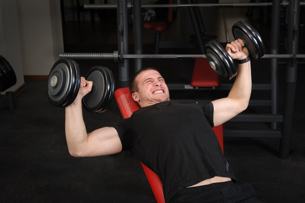 Jeune homme faisant l'entraînement de presse de banc d'inclinaison d'haltère dans la salle de gym
 - Photo, image