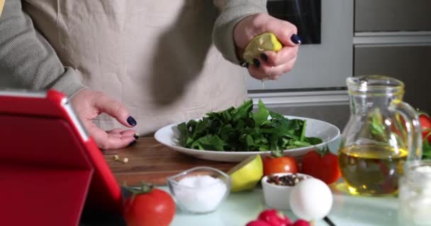 Online sanal uzmanlık kursuna göre yemek pişiren bir kadın ve dijital tarife bakıp evde mutfakta sağlıklı yemek pişirirken dokunmatik ekran tableti kullanan bir kadın. - Video, Çekim