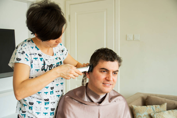 mladá žena se stříhá vlasy svého manžela doma během pandemie, zůstat doma - Fotografie, Obrázek