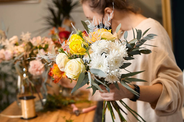 Bloemist werkt met kleuren. Bloemenverkoper kiest bloemen voor toekomstig boeket. Bloemen winkel werknemer in een masker staande in bloemenwinkel en het controleren van bloemen in glazen vaas. - Foto, afbeelding